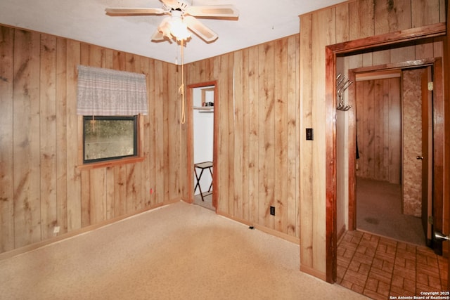 unfurnished room featuring ceiling fan, wood walls, and carpet floors