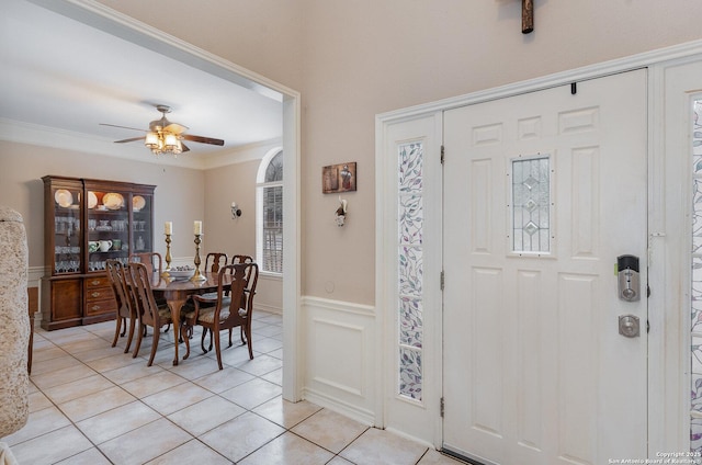 tiled foyer entrance with ceiling fan and crown molding