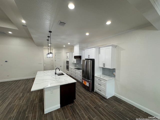 kitchen with sink, white cabinetry, stainless steel fridge, light stone countertops, and a kitchen island with sink