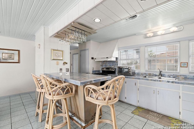 kitchen with stainless steel counters, sink, a breakfast bar area, custom range hood, and white cabinets