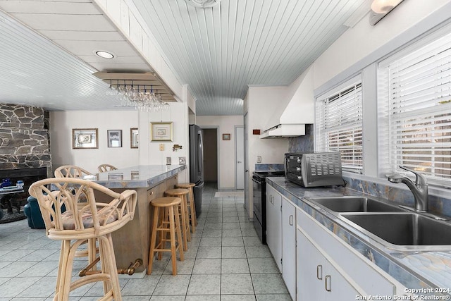 kitchen with electric range, sink, stainless steel refrigerator, a kitchen breakfast bar, and white cabinets