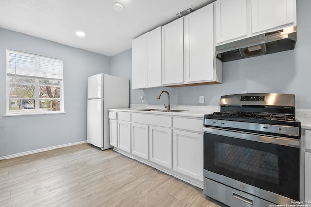 kitchen with gas stove, sink, white cabinetry, light hardwood / wood-style flooring, and white refrigerator