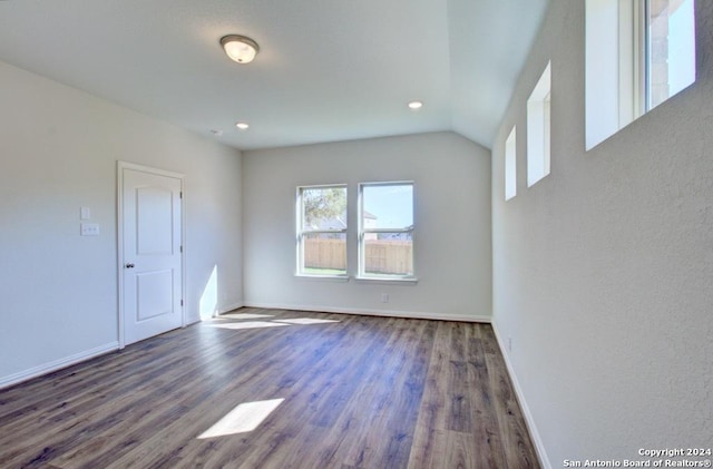 empty room featuring vaulted ceiling, plenty of natural light, and dark hardwood / wood-style flooring