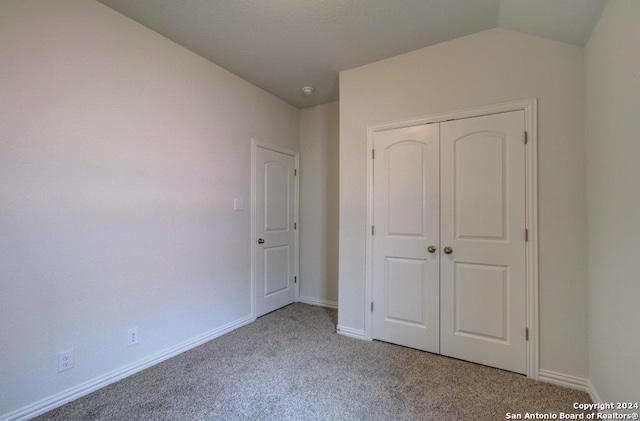 unfurnished bedroom featuring lofted ceiling, a closet, and light carpet