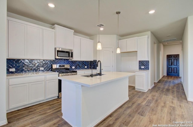 kitchen featuring an island with sink, appliances with stainless steel finishes, decorative light fixtures, white cabinets, and sink