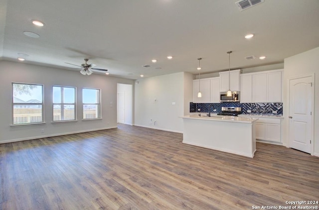 kitchen with hardwood / wood-style floors, appliances with stainless steel finishes, a kitchen island with sink, decorative light fixtures, and white cabinets