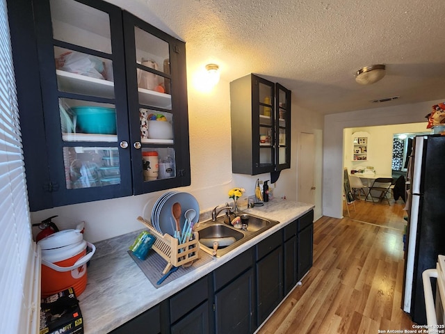 bar featuring sink, stainless steel fridge, a textured ceiling, and light hardwood / wood-style flooring