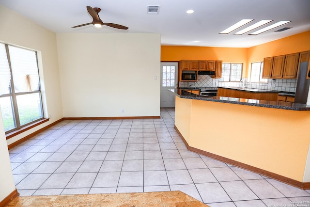 kitchen featuring a skylight, black microwave, decorative backsplash, light tile patterned floors, and kitchen peninsula