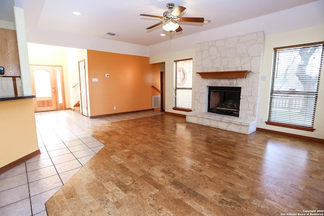 unfurnished living room featuring ceiling fan, a stone fireplace, and tile patterned flooring