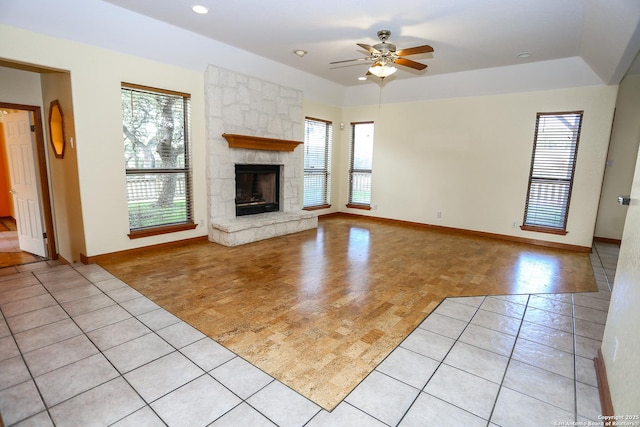 unfurnished living room with light tile patterned flooring, a stone fireplace, a wealth of natural light, and ceiling fan