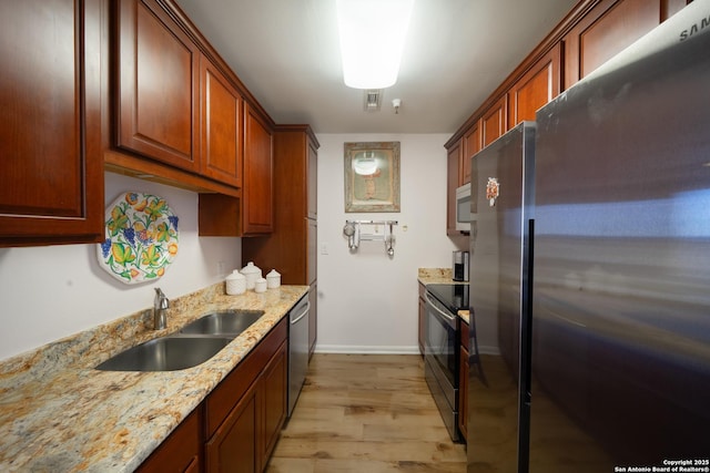 kitchen with stainless steel appliances, light stone countertops, sink, and light hardwood / wood-style floors