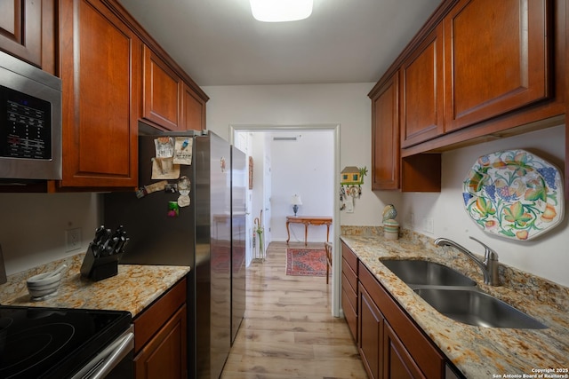 kitchen with light stone counters, stainless steel appliances, sink, and light hardwood / wood-style flooring