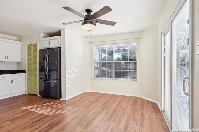 kitchen with black refrigerator, hardwood / wood-style flooring, a wealth of natural light, and white cabinets