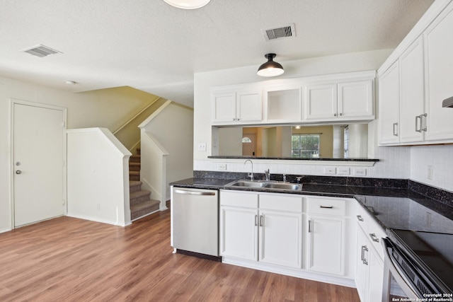 kitchen with stainless steel dishwasher, sink, white cabinets, dark stone counters, and hardwood / wood-style floors