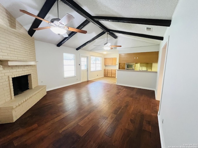 unfurnished living room with ceiling fan, a brick fireplace, lofted ceiling with beams, wood-type flooring, and a textured ceiling