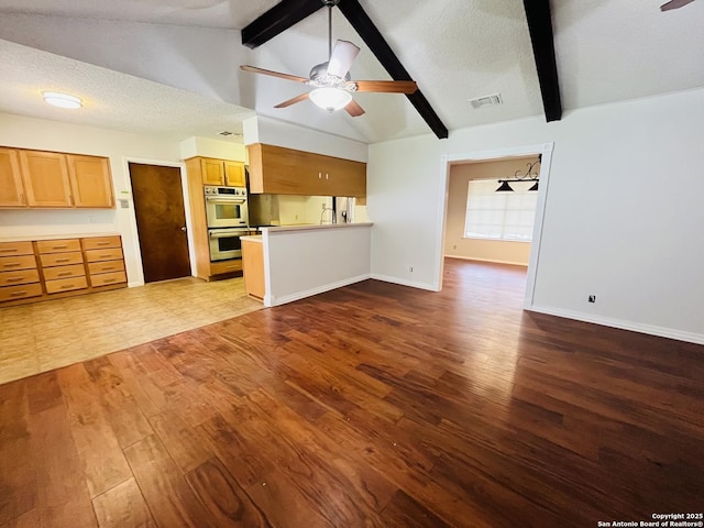 unfurnished living room featuring a textured ceiling, ceiling fan, wood-type flooring, and lofted ceiling with beams