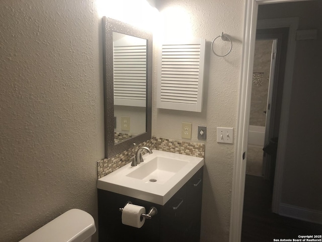 bathroom featuring toilet, vanity, and backsplash