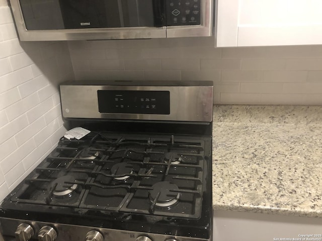 room details with white cabinets, backsplash, light stone countertops, and stainless steel appliances