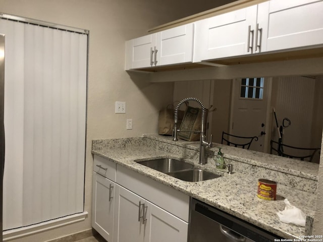 kitchen featuring light stone countertops, white cabinetry, stainless steel dishwasher, and sink