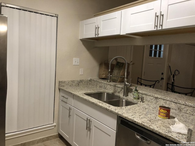 kitchen with light stone countertops, white cabinetry, dishwasher, and sink