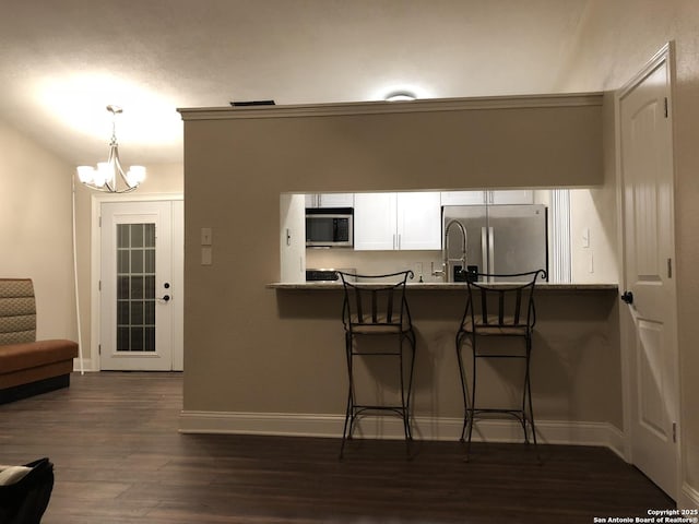 kitchen featuring appliances with stainless steel finishes, a kitchen breakfast bar, hanging light fixtures, light stone countertops, and white cabinets