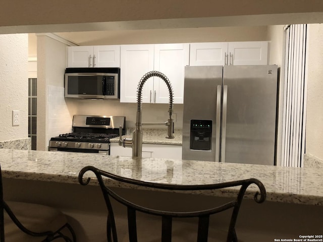 kitchen with tasteful backsplash, appliances with stainless steel finishes, light stone counters, and white cabinetry