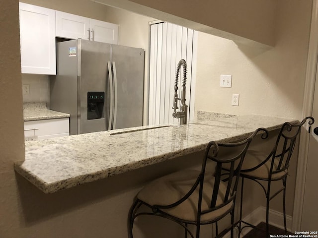 kitchen featuring a breakfast bar area, kitchen peninsula, stainless steel fridge, and white cabinetry