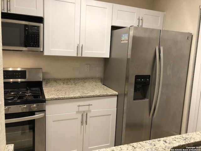 kitchen with light stone counters, backsplash, white cabinetry, and appliances with stainless steel finishes