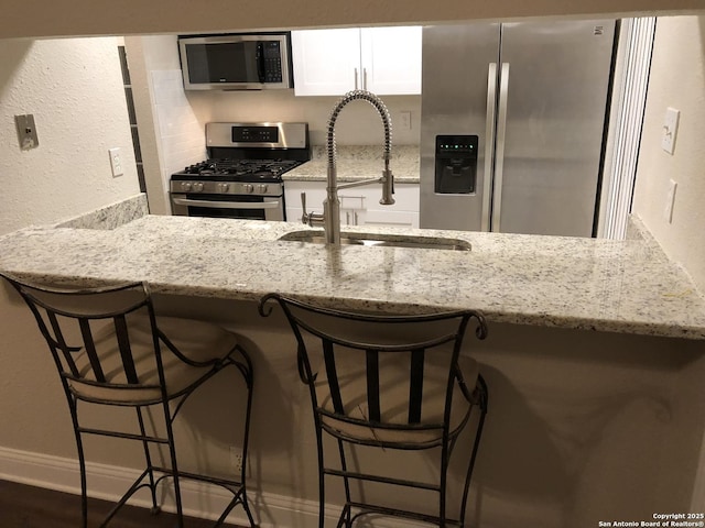 kitchen with a breakfast bar, sink, stainless steel appliances, white cabinets, and light stone counters