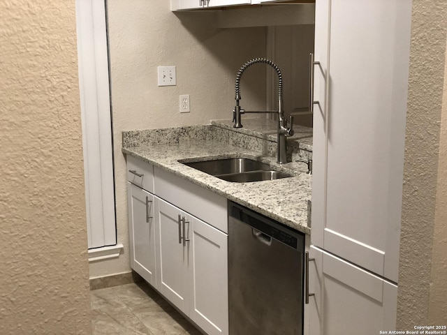 kitchen featuring light stone countertops, white cabinetry, stainless steel dishwasher, and sink