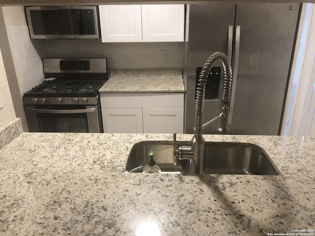 kitchen with appliances with stainless steel finishes, sink, white cabinets, and light stone countertops