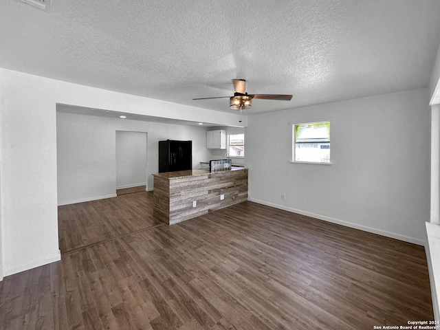 unfurnished living room with ceiling fan, dark wood-type flooring, and a textured ceiling