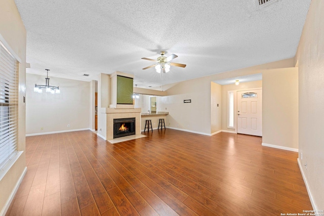 unfurnished living room featuring wood-type flooring, a large fireplace, plenty of natural light, and ceiling fan with notable chandelier