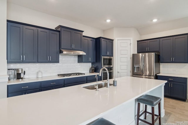 kitchen with appliances with stainless steel finishes, a kitchen bar, tasteful backsplash, an island with sink, and sink