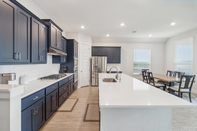 kitchen featuring backsplash, sink, light hardwood / wood-style flooring, a kitchen island with sink, and appliances with stainless steel finishes