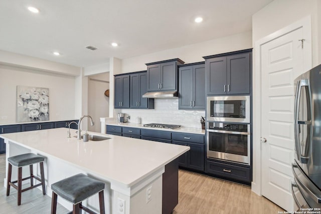 kitchen featuring decorative backsplash, a kitchen bar, sink, a kitchen island with sink, and appliances with stainless steel finishes