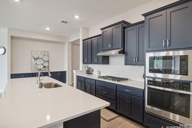 kitchen with an island with sink, decorative backsplash, sink, stainless steel gas cooktop, and built in microwave