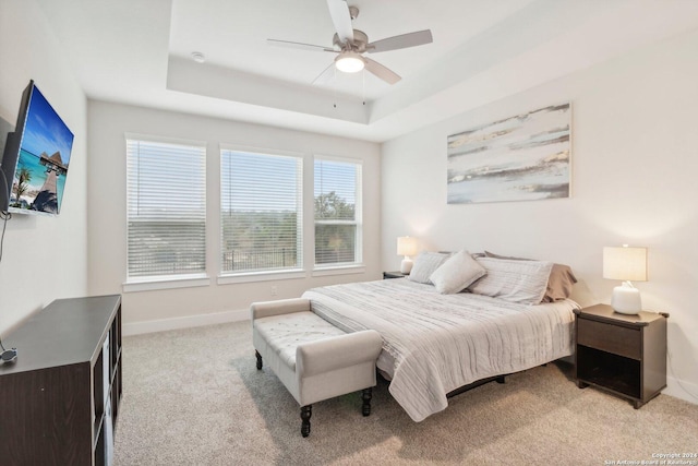 bedroom featuring light carpet, ceiling fan, a raised ceiling, and multiple windows