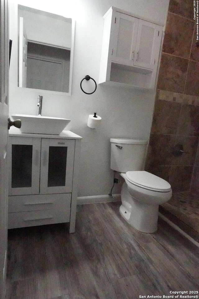 bathroom featuring toilet, tiled shower, hardwood / wood-style floors, and vanity