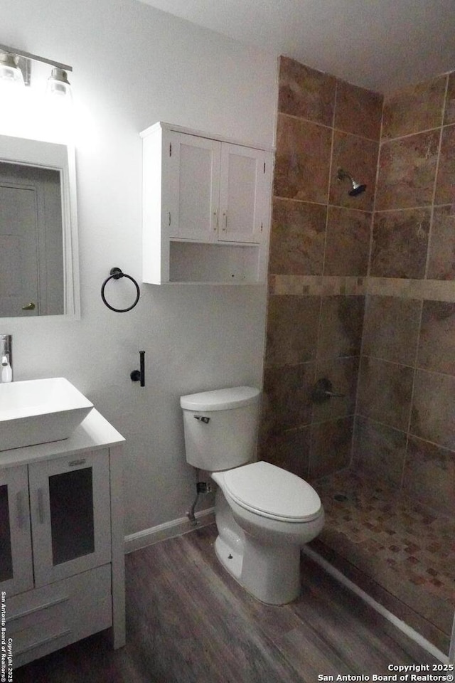 bathroom with toilet, vanity, tiled shower, and hardwood / wood-style flooring