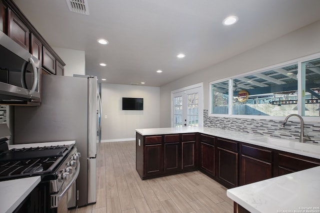 kitchen with kitchen peninsula, appliances with stainless steel finishes, backsplash, light wood-type flooring, and sink