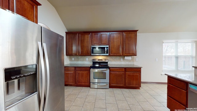 kitchen with stainless steel appliances, tasteful backsplash, light tile patterned flooring, lofted ceiling, and stone counters