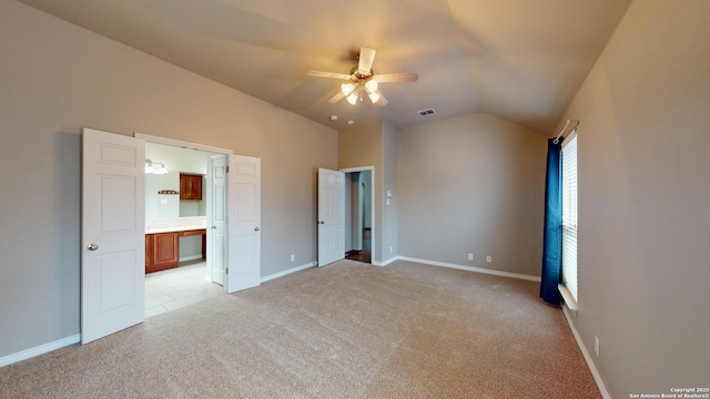 unfurnished bedroom featuring ceiling fan, ensuite bath, light carpet, and vaulted ceiling