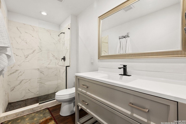 bathroom featuring hardwood / wood-style flooring, toilet, tiled shower, and vanity