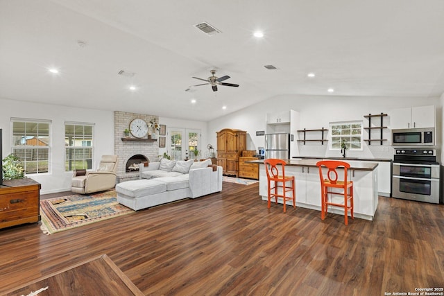 living room featuring dark wood-type flooring, ceiling fan, sink, vaulted ceiling, and a brick fireplace