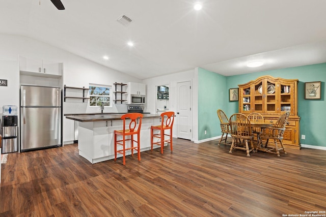 kitchen with a kitchen breakfast bar, dark wood-type flooring, appliances with stainless steel finishes, and white cabinetry