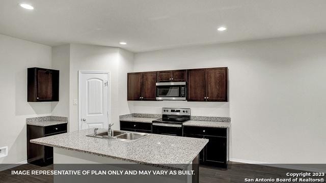 kitchen with dark brown cabinetry, stainless steel appliances, an island with sink, sink, and dark hardwood / wood-style floors