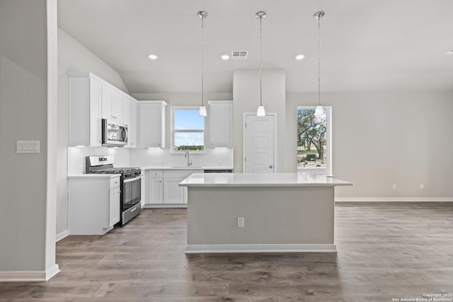 kitchen with stainless steel appliances, decorative light fixtures, a kitchen island, white cabinets, and sink