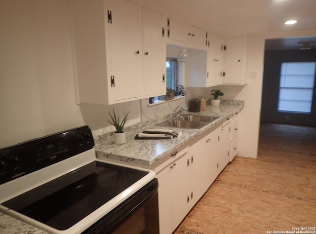 kitchen featuring black range with electric stovetop, light stone countertops, sink, and white cabinets