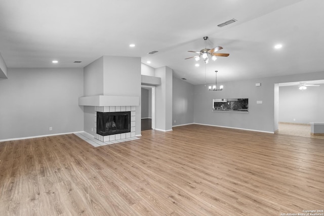 unfurnished living room with ceiling fan with notable chandelier, light wood-type flooring, lofted ceiling, and a fireplace